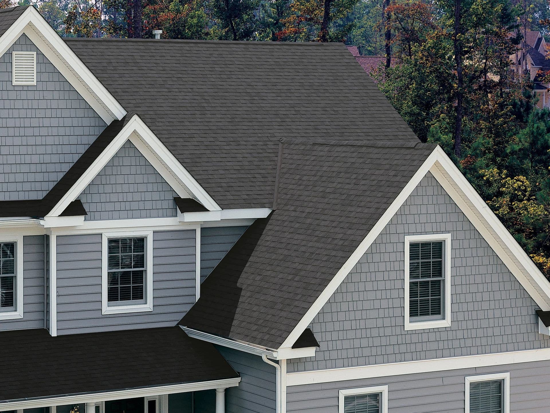 Gray house with gabled roof features dark gray shingles and white trim. Surrounded by trees, conveying a serene, suburban atmosphere.