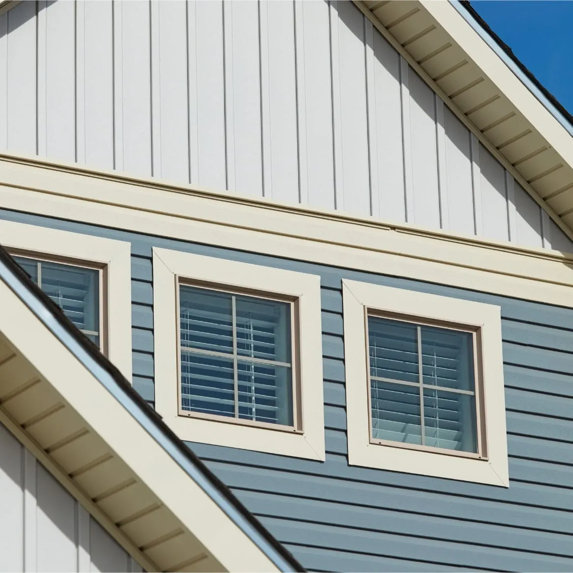 Close-up of a house exterior showing blue horizontal siding and three white-framed windows with shutters, creating a clean and modern look.